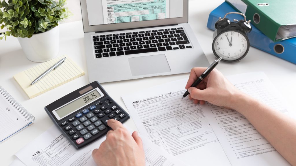 Professional accountant working on tax forms with calculator, laptop, and office supplies, providing expert tax preparation and financial services for small businesses and individuals in the UK.