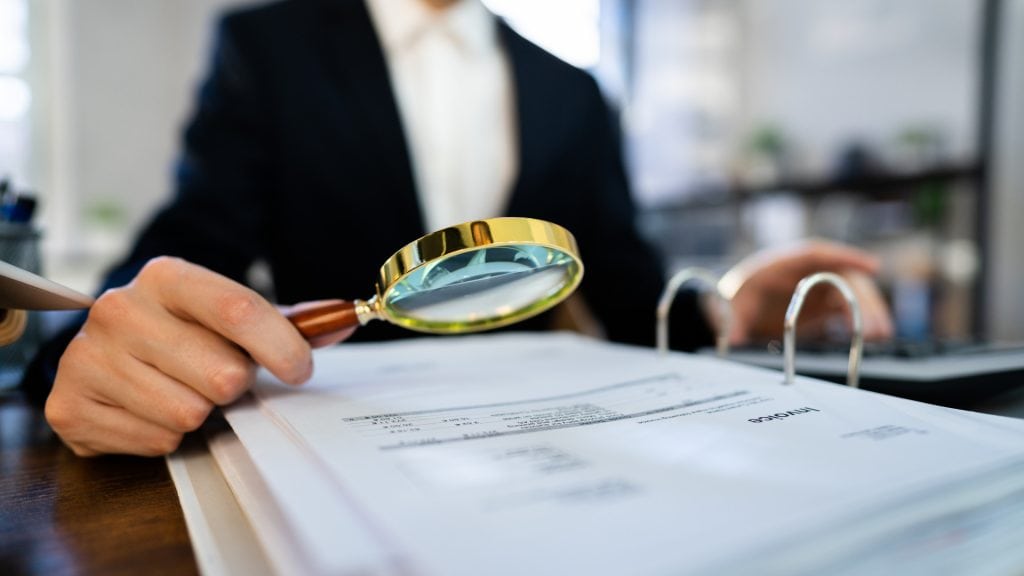 Magnifying glass inspecting financial documents at an accounting firm, representing thorough financial analysis and expert accounting services in the UK.