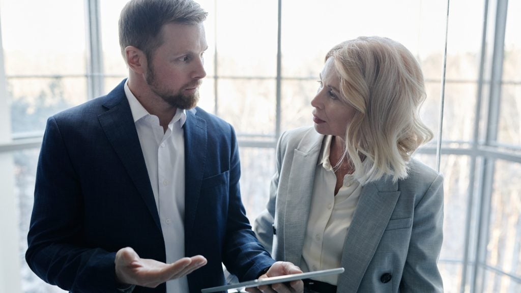 Professional accountants discussing finances using a tablet in a bright office environment.