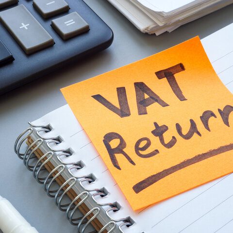 VAT return deadline and tax compliance documentation for UK businesses, highlighted on an orange sticky note placed on a desk with calculator and stationery.