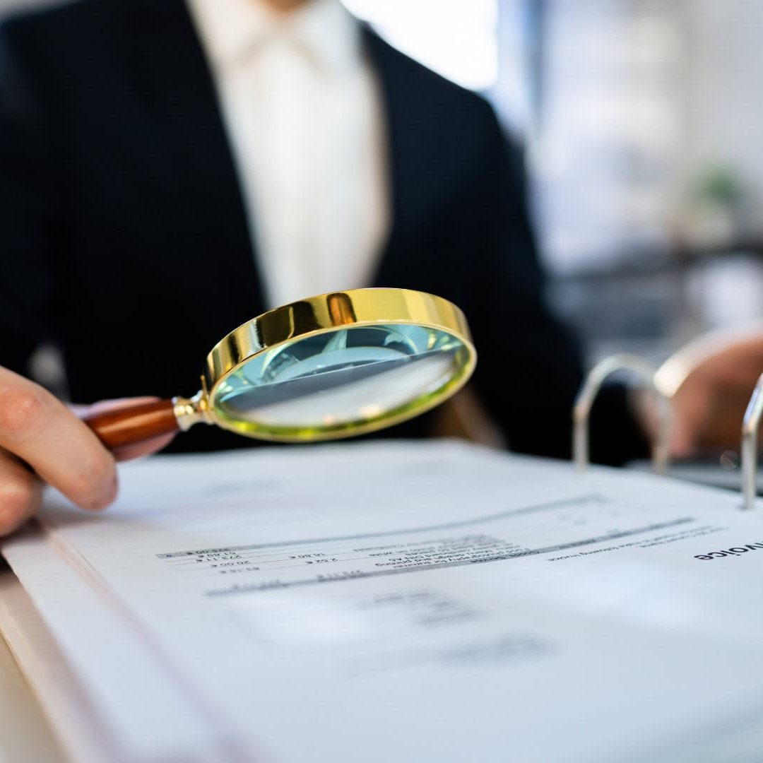 Magnifying glass inspecting financial documents at an accounting firm, representing thorough financial analysis and expert accounting services in the UK.