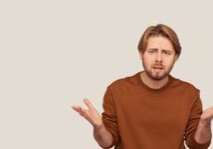 Confused man shrugging with open hands, representing accounting or financial questions, in a brown sweatshirt against a plain beige background.