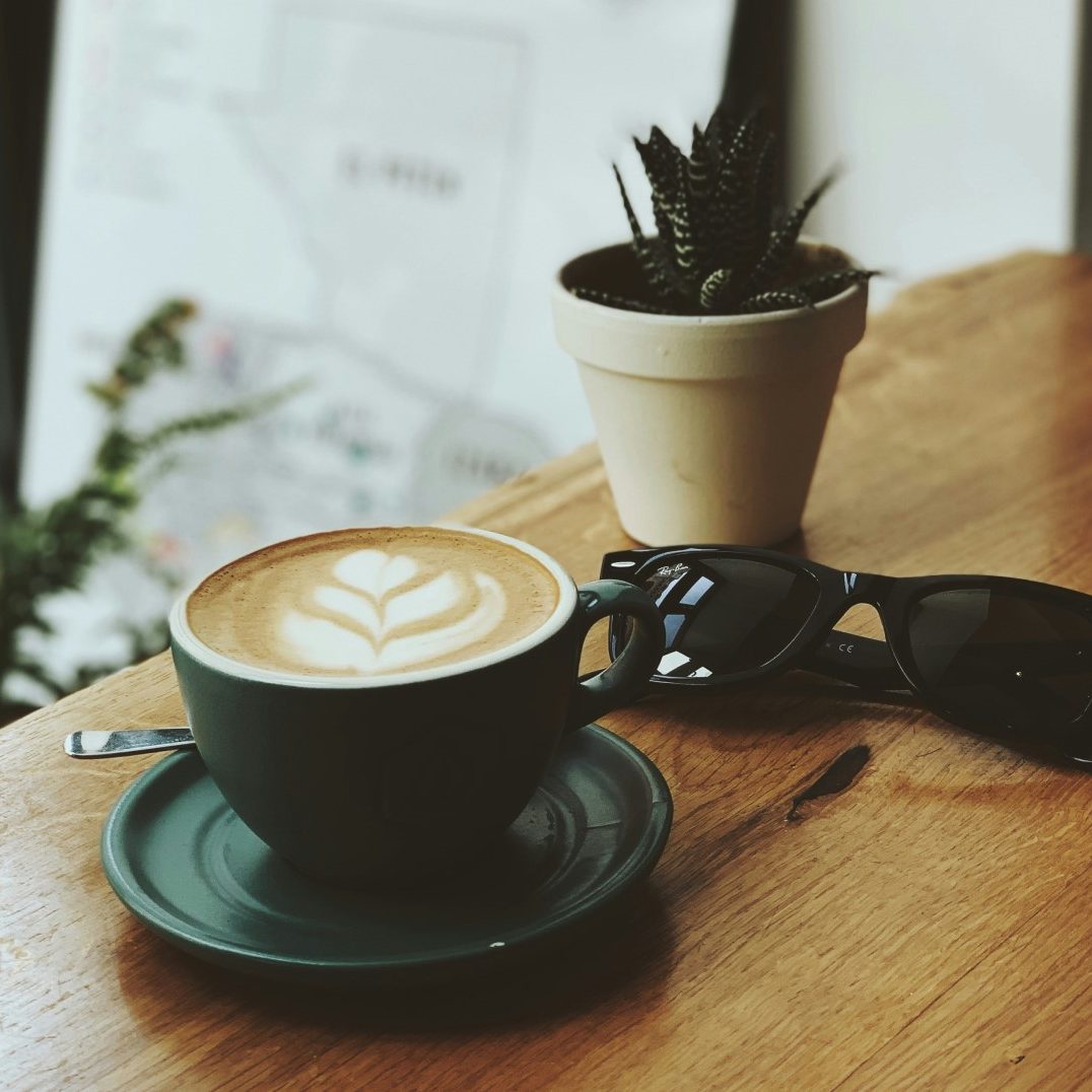 Coffee with latte art, sunglasses, and a potted succulent on a wooden table at GMS Accountants office or café.